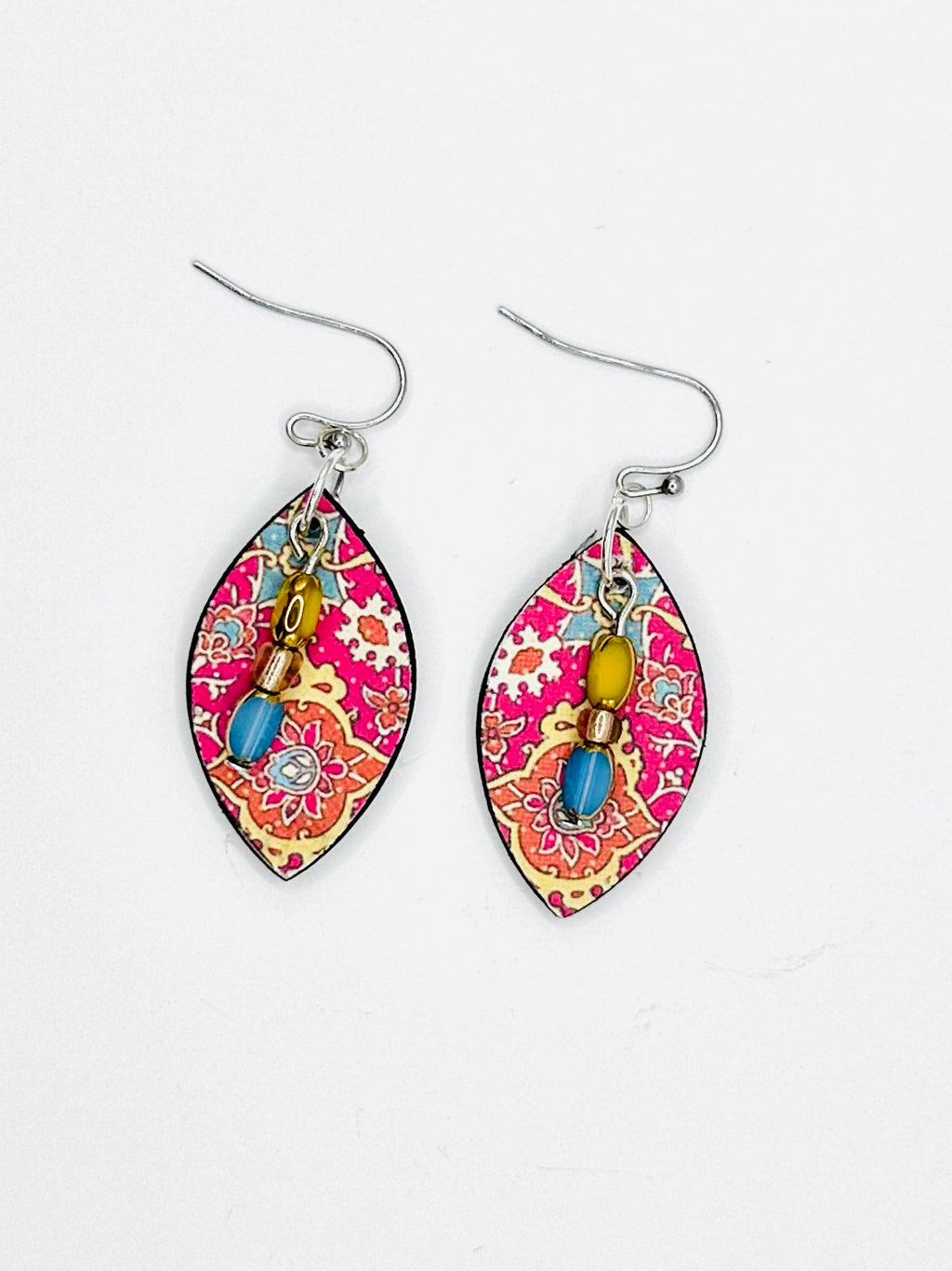 A pair of dangling earrings with silver fishhook wires and teardrop-shaped charms featuring a pink, red, and gold paisley pattern with small colorful bead accents, displayed on a white surface.