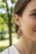 A pair of dangling earrings .The earrings have a black backing with a colorful red, pink, and blue patterned design, and each features a central bead in yellow and light blue with a small gold-tone