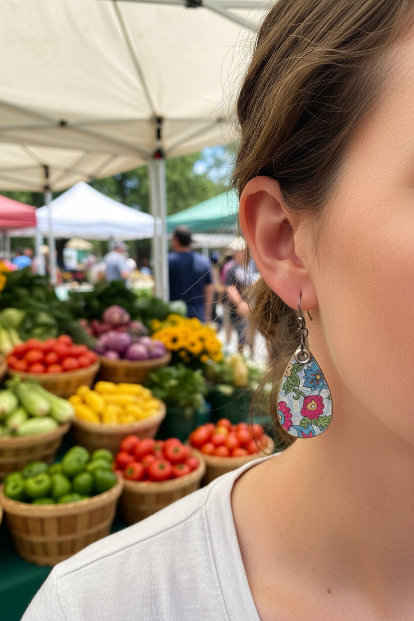 Teardrop-shaped dangle earrings with a colorful floral print on a light blue background, hanging from silver hypoallergenic fishhook wires.