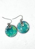 A pair of handmade round drop earrings featuring a marbled turquoise, teal, and green resin face with tiny gold & silver flecks.  Hypoallergenic silver fishhook wires.  Lightweight 