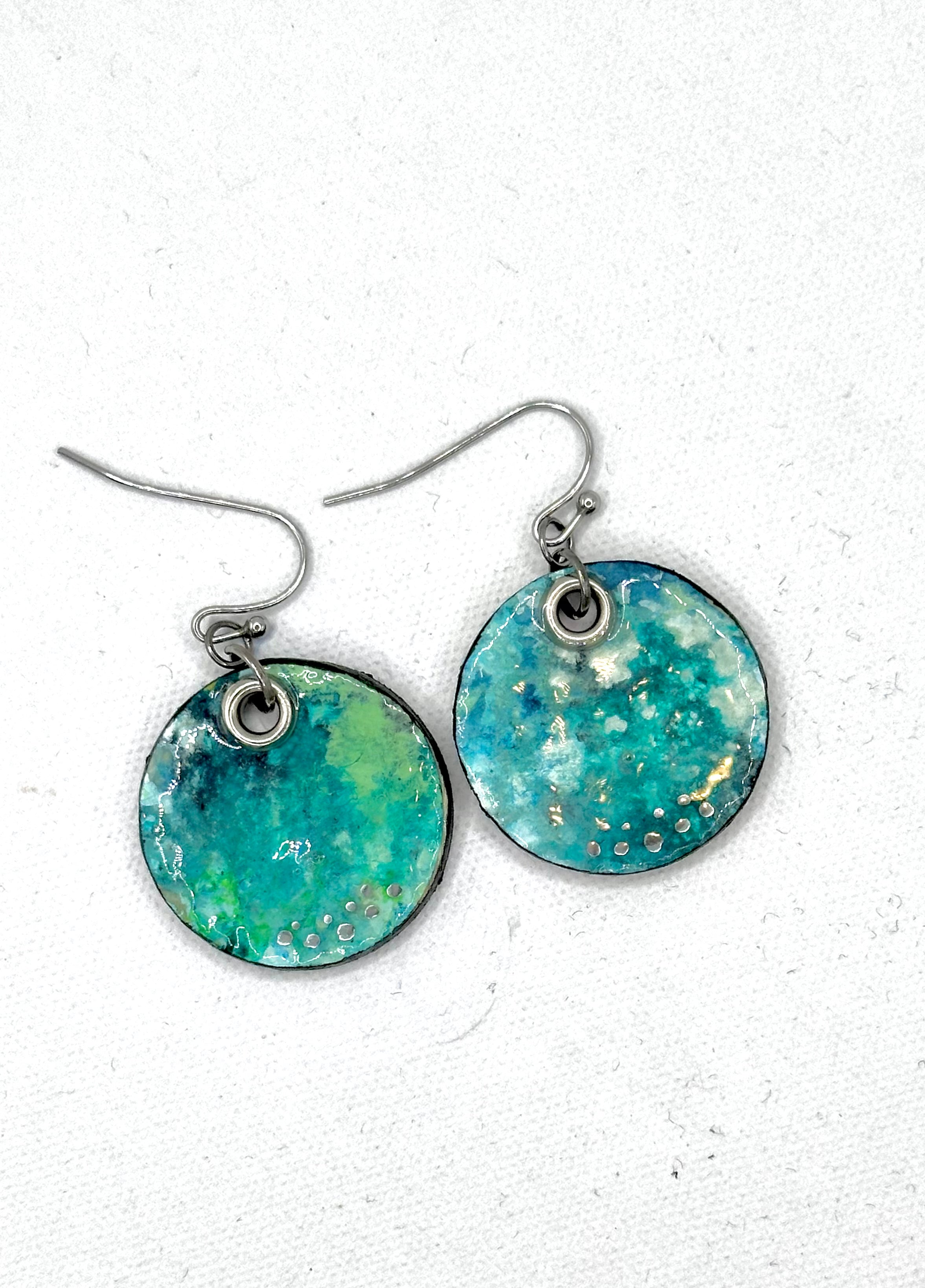 A pair of handmade round drop earrings featuring a marbled turquoise, teal, and green resin face with tiny gold & silver flecks.  Hypoallergenic silver fishhook wires.  Lightweight 