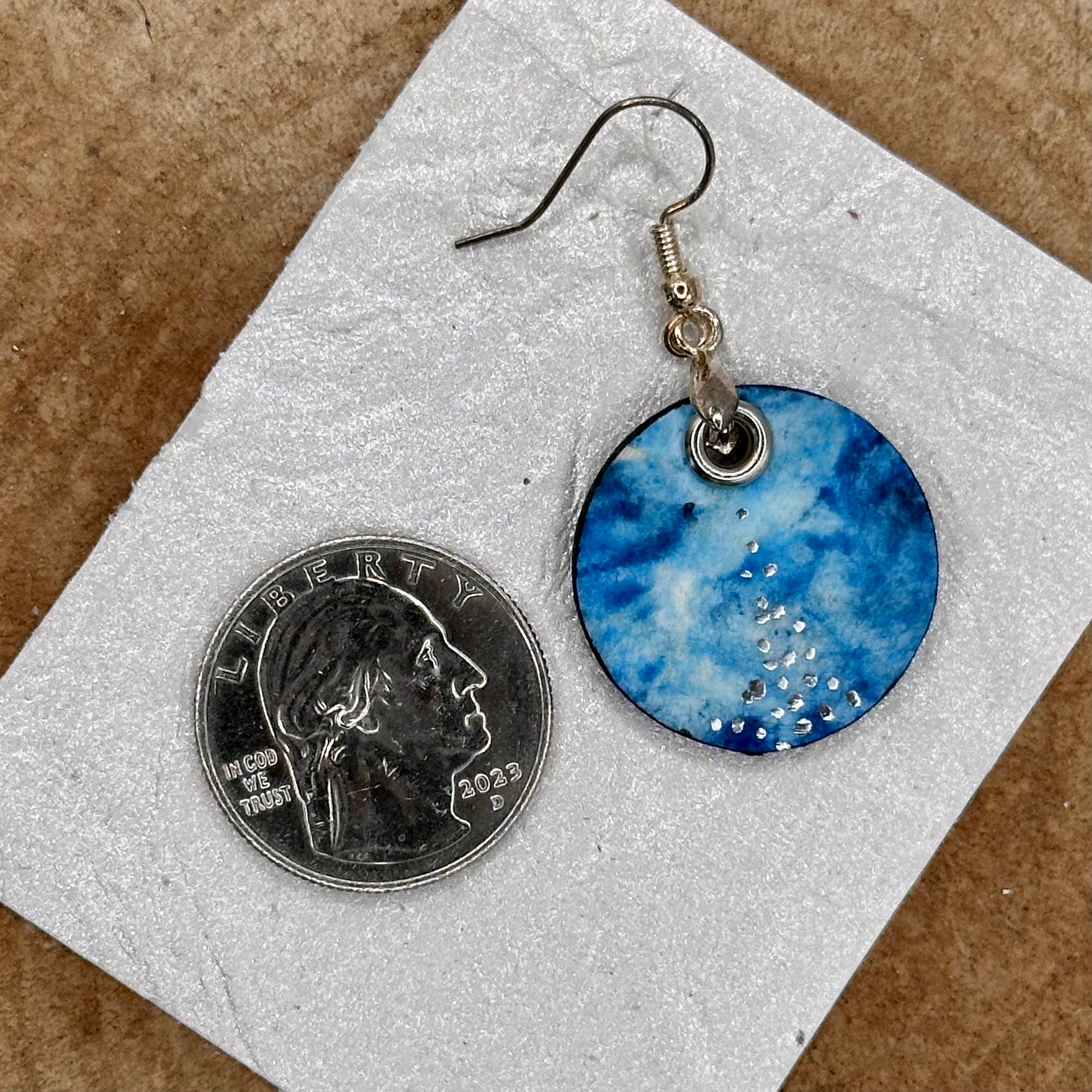 A pair of handmade dangle earrings with a hand painted blue and teal marbled pattern, featuring small silver accents and silver tone&nbsp; &nbsp;Sealed with a protective glaze.&nbsp; Hypoallergenic hooks.