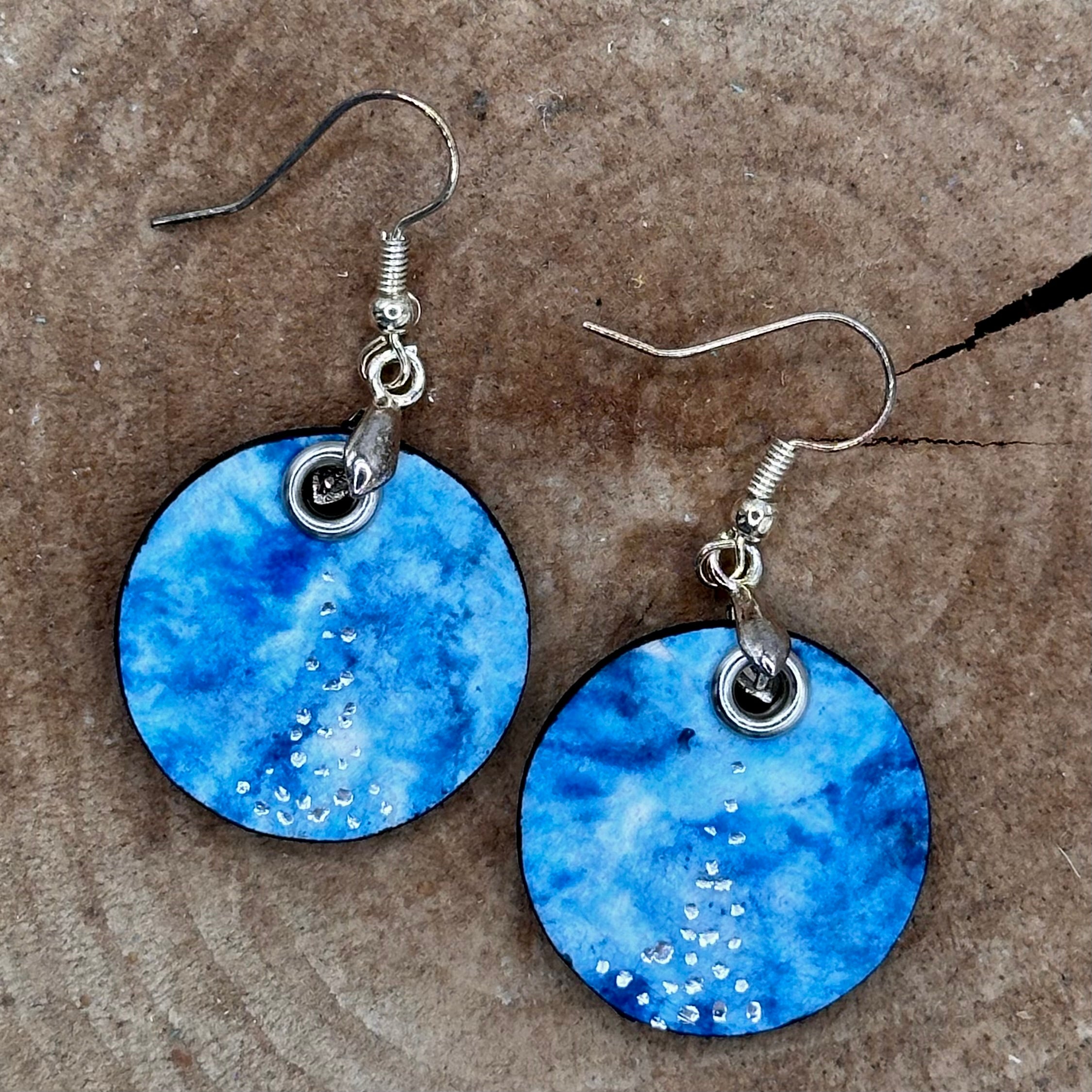 A pair of handmade dangle earrings with a hand painted blue and teal marbled pattern, featuring small silver accents and silver tone&nbsp; &nbsp;Sealed with a protective glaze.&nbsp; Hypoallergenic hooks.
