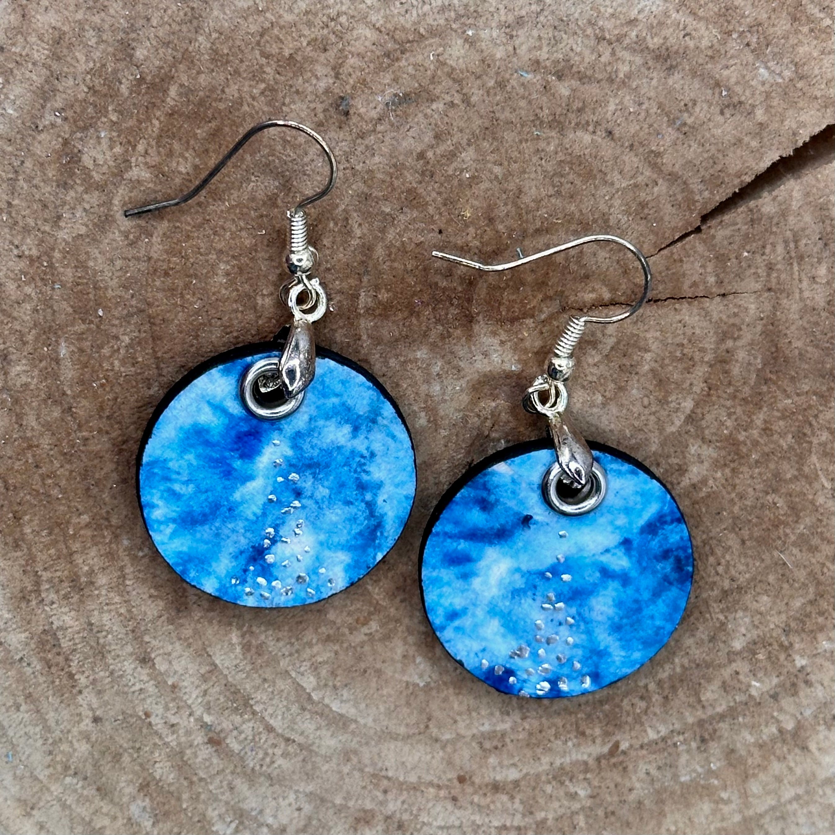 A pair of handmade dangle earrings with a hand painted blue and teal marbled pattern, featuring small silver accents and silver tone&nbsp; &nbsp;Sealed with a protective glaze.&nbsp; Hypoallergenic hooks.
