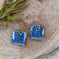 A pair of handmade square denim dangle earrings with silver fishhook wires and green teardrop charm.