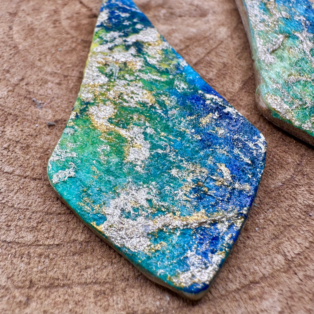 Hand painted earrings in marbled teal, green, and gold textured with silver-tone fishhook wires. Sealed with a protective mat varnish. &nbsp;Hypoallergenic and light as a feather.&nbsp; 2” long not including earring wire.