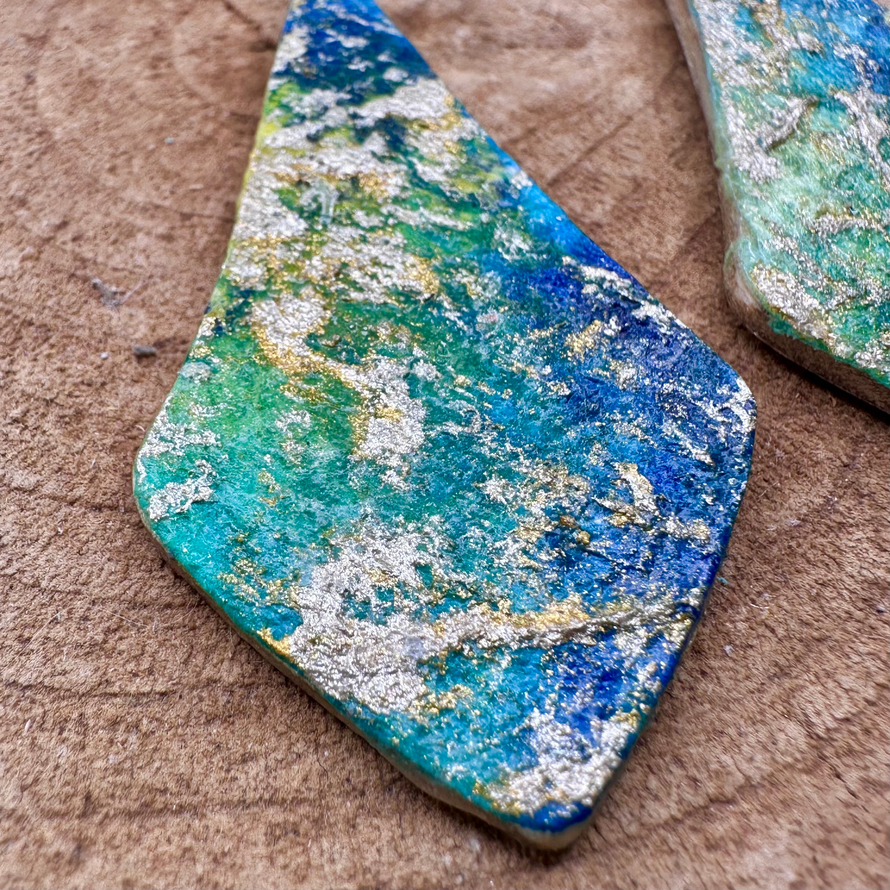 Hand painted earrings in marbled teal, green, and gold textured with silver-tone fishhook wires. Sealed with a protective mat varnish. &nbsp;Hypoallergenic and light as a feather.&nbsp; 2” long not including earring wire.