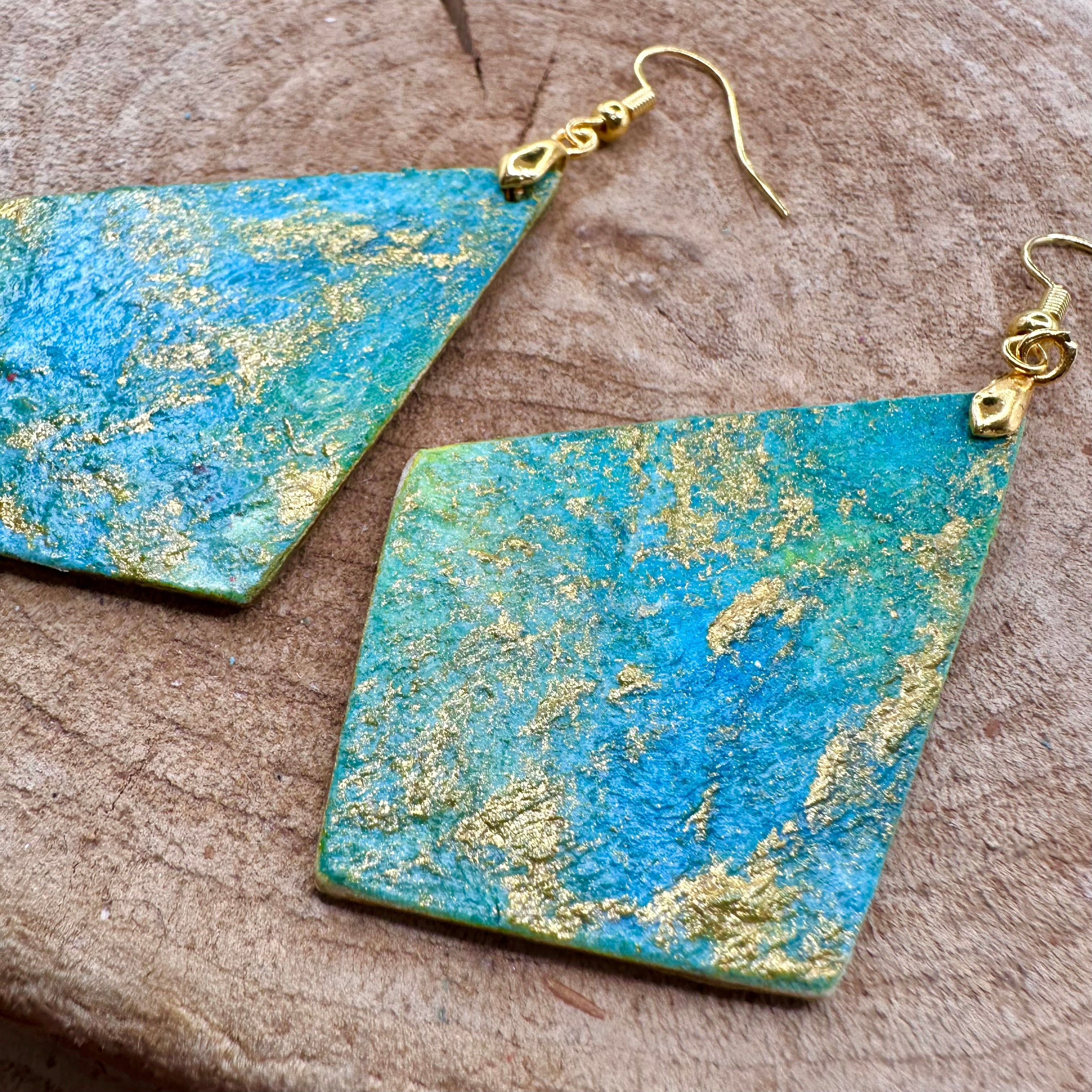 Hand painted earrings in marbled teal, green, and gold textured with gold-tone fishhook wires and diamond-shaped pendants. Sealed with a protective mat varnish. Hypoallergenic and light as a feather.  2” long not including earring wire.