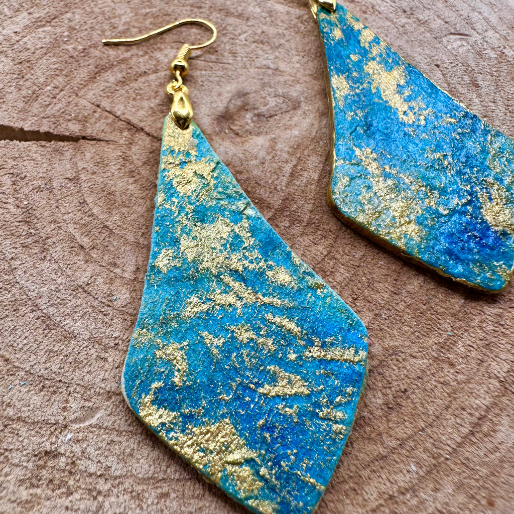 Hand painted earrings in marbled teal, green, and gold textured with gold-tone fishhook wires and diamond-shaped pendants. Sealed with a protective mat varnish. Hypoallergenic and light as a feather. 2” long not including earring wire.