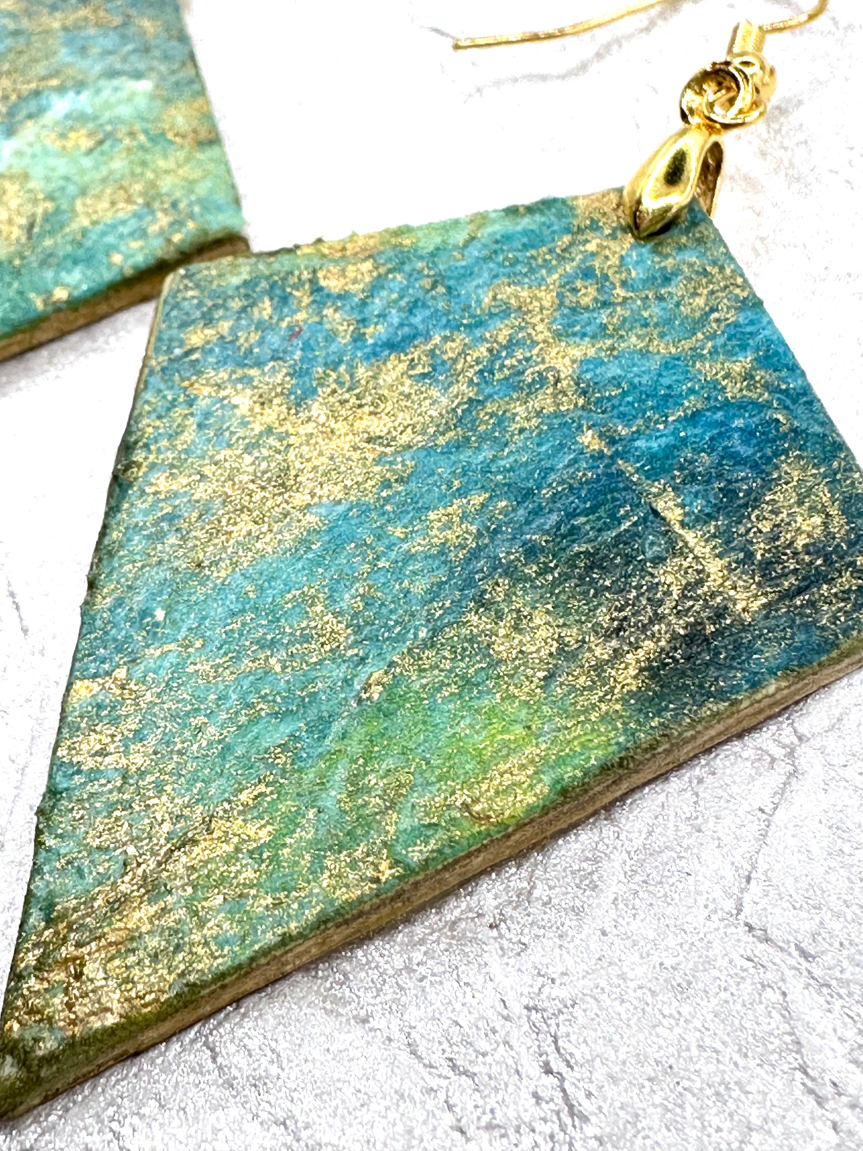 Hand painted earrings in marbled teal, green, and gold textured with gold-tone fishhook wires and diamond-shaped pendants. Hypoallergenic and light as a feather.   2" long without the earring wire.